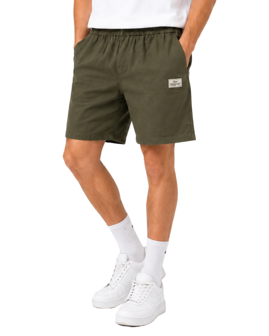 A person wearing olive green drawstring shorts with a small white brand patch on the left thigh, styled with a white t-shirt, white socks, and white sneakers against a plain white background.